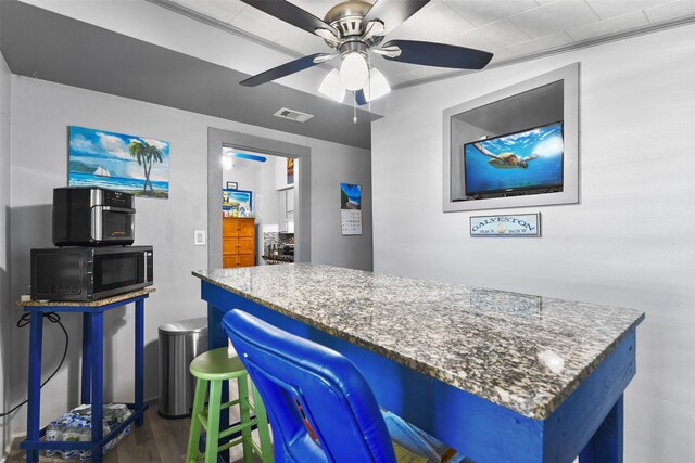 interior space featuring stone counters, a breakfast bar, ceiling fan, and dark hardwood / wood-style floors