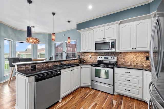 kitchen featuring white cabinetry, sink, hanging light fixtures, appliances with stainless steel finishes, and ornamental molding