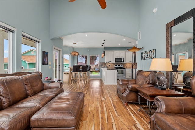 living room featuring ceiling fan, light wood-type flooring, and a towering ceiling