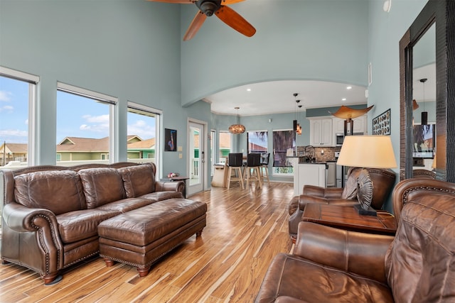 living room with a high ceiling, light hardwood / wood-style flooring, plenty of natural light, and ceiling fan