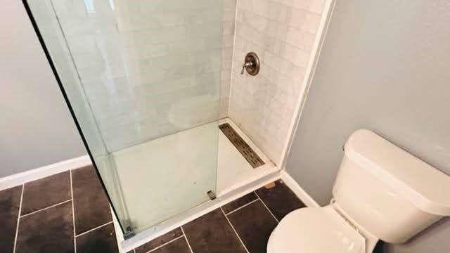 bathroom featuring tile patterned floors, toilet, and tiled shower