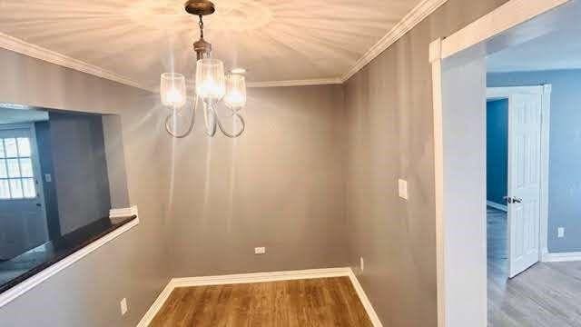 unfurnished dining area with crown molding, hardwood / wood-style floors, and an inviting chandelier