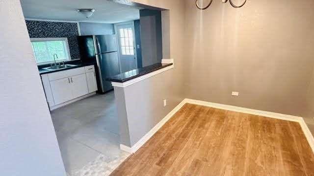 kitchen with white cabinets, light hardwood / wood-style floors, black fridge, and sink