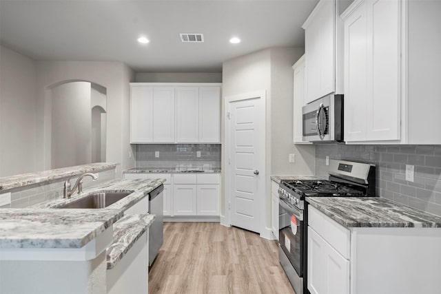 kitchen featuring sink, light hardwood / wood-style flooring, decorative backsplash, appliances with stainless steel finishes, and white cabinetry