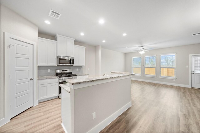 kitchen featuring backsplash, white cabinets, a center island with sink, ceiling fan, and stainless steel appliances