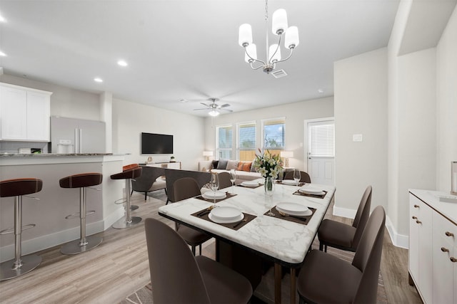 dining room with ceiling fan with notable chandelier and light hardwood / wood-style flooring