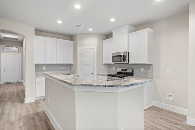 kitchen with light stone counters, white cabinetry, an island with sink, and appliances with stainless steel finishes