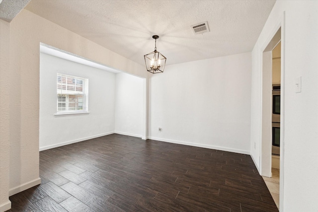 empty room with dark wood-type flooring, a textured ceiling, and an inviting chandelier