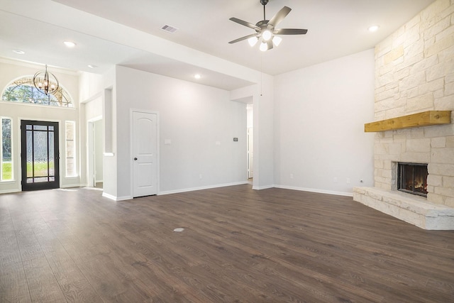 unfurnished living room with ceiling fan with notable chandelier, a stone fireplace, dark hardwood / wood-style flooring, and a towering ceiling