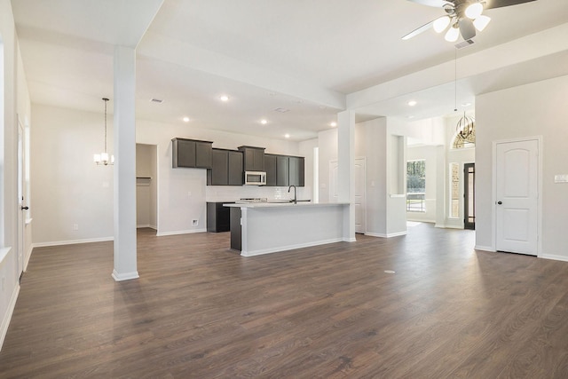 kitchen with sink, hanging light fixtures, dark wood-type flooring, and an island with sink