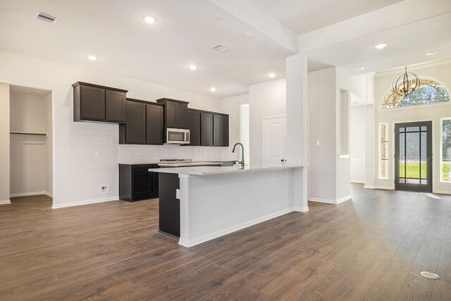 kitchen featuring light stone countertops, dark hardwood / wood-style flooring, tasteful backsplash, a chandelier, and an island with sink