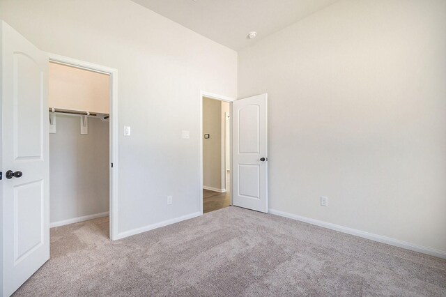 unfurnished bedroom featuring light carpet, a closet, a spacious closet, and lofted ceiling