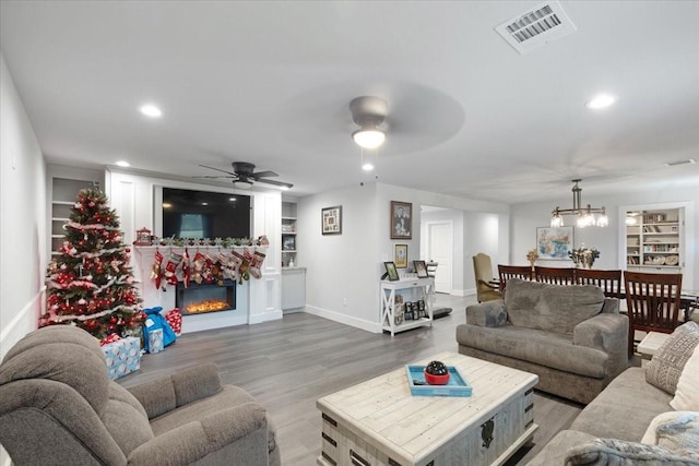 living room with hardwood / wood-style flooring, built in shelves, and ceiling fan with notable chandelier