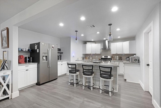 kitchen with wall chimney exhaust hood, light stone counters, pendant lighting, white cabinets, and appliances with stainless steel finishes