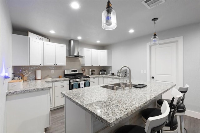 kitchen with sink, wall chimney exhaust hood, decorative light fixtures, gas stove, and white cabinetry