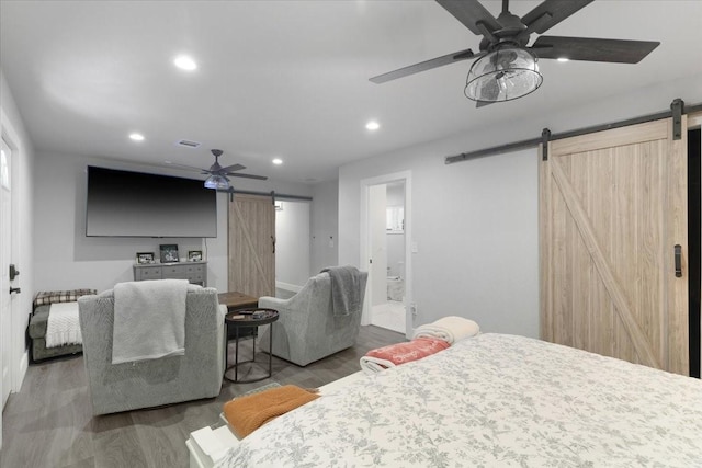 bedroom with a barn door, ceiling fan, ensuite bathroom, and hardwood / wood-style flooring