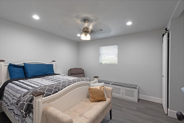 bedroom featuring a barn door, ceiling fan, and dark hardwood / wood-style floors