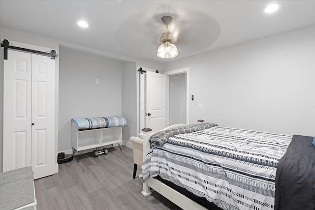 bedroom featuring ceiling fan, a barn door, light hardwood / wood-style flooring, and a closet