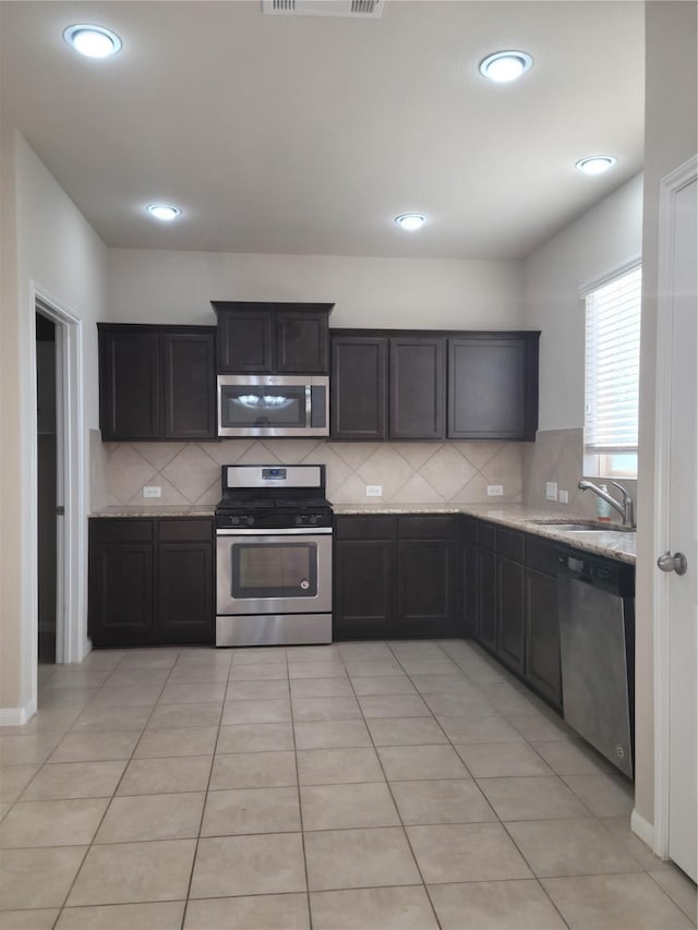 kitchen with sink, light tile patterned floors, tasteful backsplash, light stone counters, and stainless steel appliances