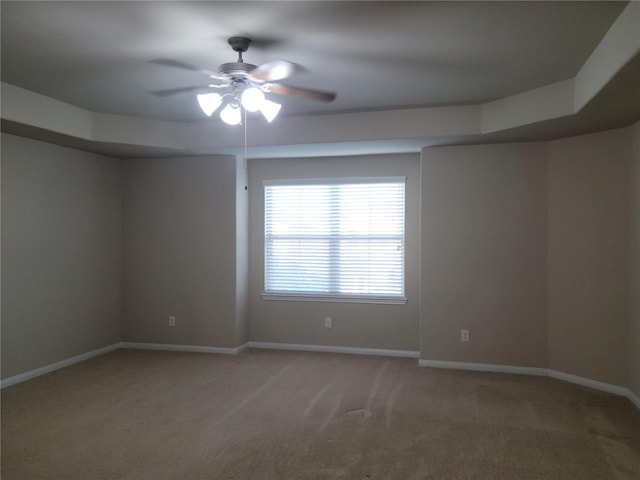 carpeted spare room with a raised ceiling and ceiling fan