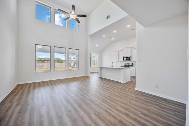 unfurnished living room with ceiling fan, sink, a high ceiling, and light wood-type flooring