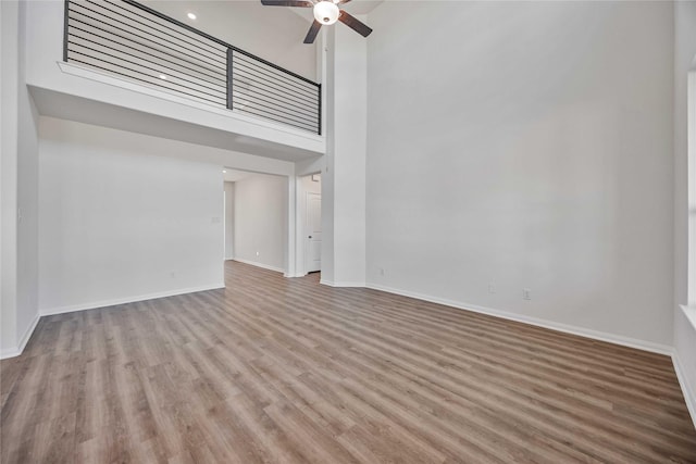 unfurnished living room with ceiling fan, light wood-type flooring, and a high ceiling