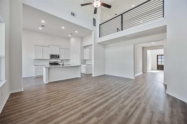 unfurnished living room with ceiling fan, sink, a towering ceiling, and light hardwood / wood-style floors