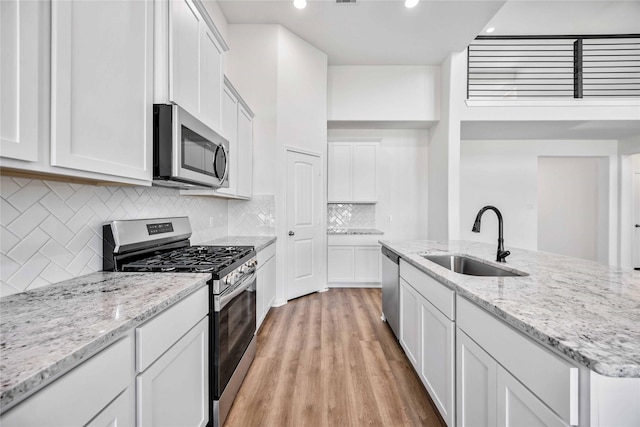 kitchen with white cabinetry, sink, stainless steel appliances, light stone counters, and light hardwood / wood-style flooring