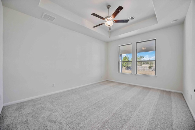 carpeted empty room with a raised ceiling and ceiling fan