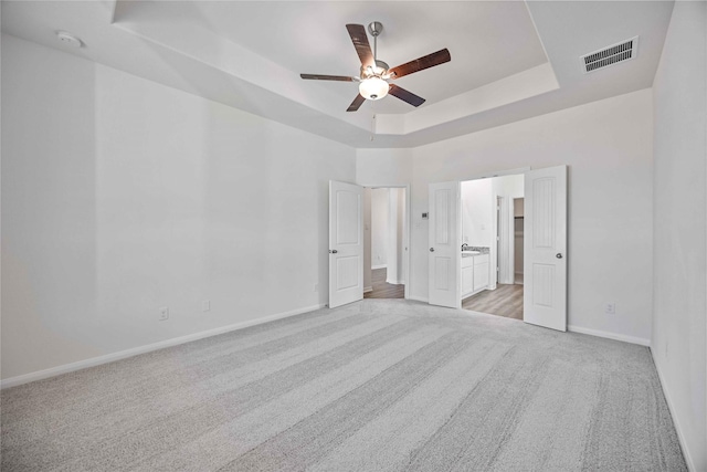 unfurnished bedroom with ceiling fan, a raised ceiling, light colored carpet, and a high ceiling