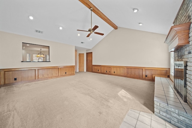 unfurnished living room featuring ceiling fan with notable chandelier, light colored carpet, wooden walls, beam ceiling, and a fireplace