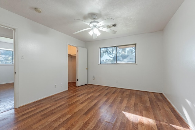 unfurnished bedroom featuring multiple windows, a spacious closet, ceiling fan, and dark wood-type flooring