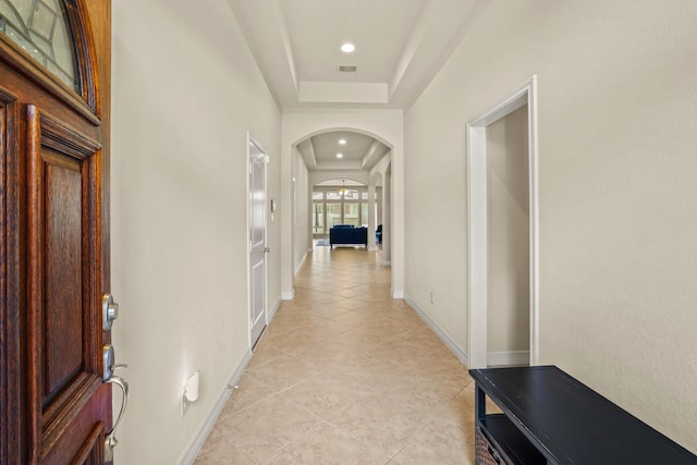 hall with a tray ceiling and light tile patterned flooring