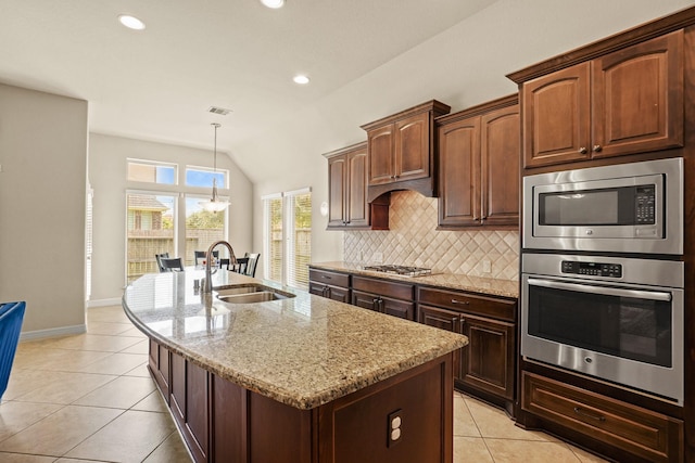 kitchen with a center island with sink, light stone countertops, sink, and vaulted ceiling