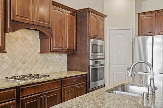 kitchen featuring appliances with stainless steel finishes, tasteful backsplash, light stone counters, and sink