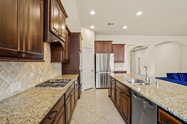 kitchen featuring backsplash, light stone counters, stainless steel appliances, sink, and light tile patterned floors