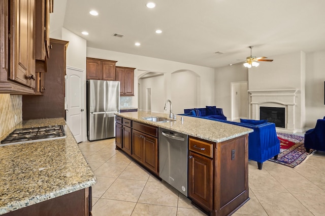 kitchen with backsplash, stainless steel appliances, ceiling fan, sink, and an island with sink