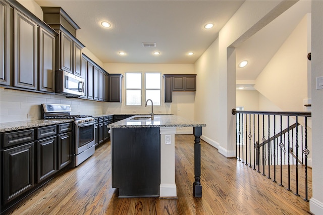 kitchen with light stone countertops, sink, a kitchen island with sink, decorative backsplash, and appliances with stainless steel finishes