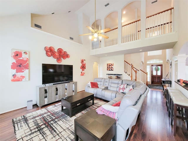 living room featuring dark hardwood / wood-style floors, ceiling fan, ornate columns, and a high ceiling