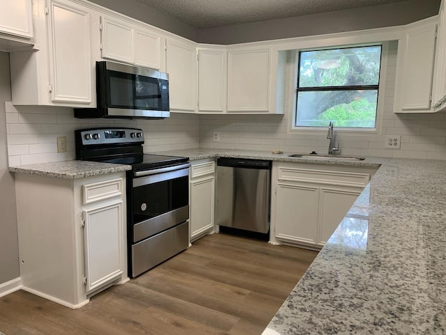 kitchen featuring white cabinetry, appliances with stainless steel finishes, wood-type flooring, light stone countertops, and sink