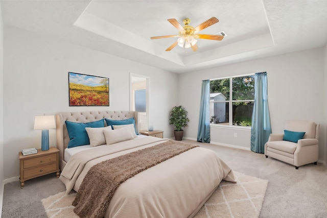 carpeted bedroom with a raised ceiling and ceiling fan