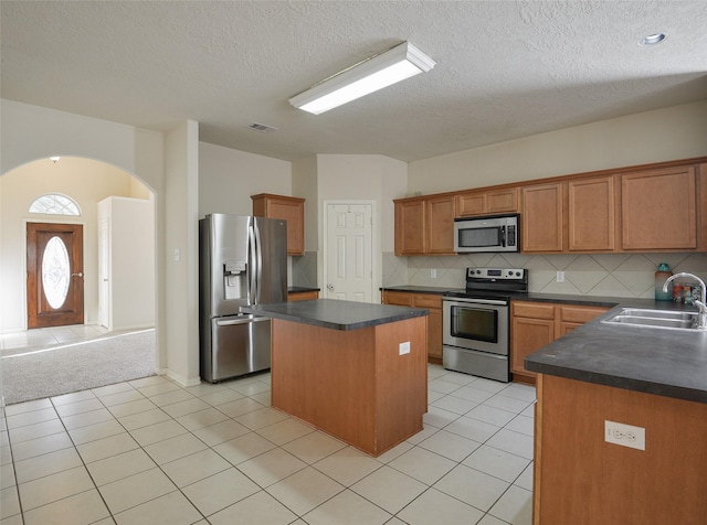 kitchen with decorative backsplash, appliances with stainless steel finishes, sink, a center island, and light tile patterned flooring