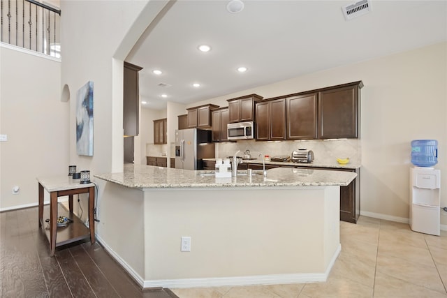 kitchen featuring a kitchen bar, kitchen peninsula, light stone counters, and stainless steel appliances