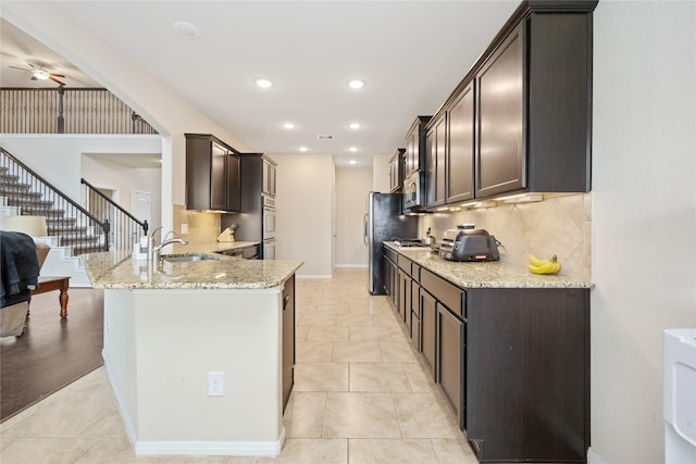 kitchen with ceiling fan, sink, light stone counters, dark brown cabinets, and appliances with stainless steel finishes