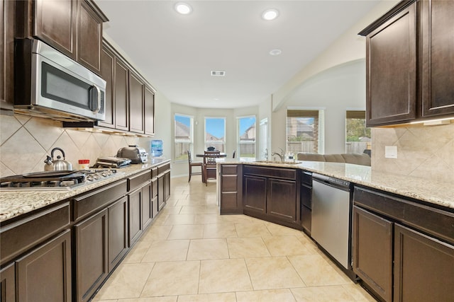 kitchen with light stone countertops, sink, decorative backsplash, dark brown cabinets, and appliances with stainless steel finishes