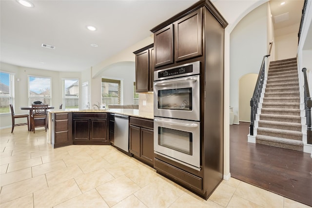 kitchen featuring sink, light tile patterned floors, appliances with stainless steel finishes, light stone counters, and dark brown cabinetry