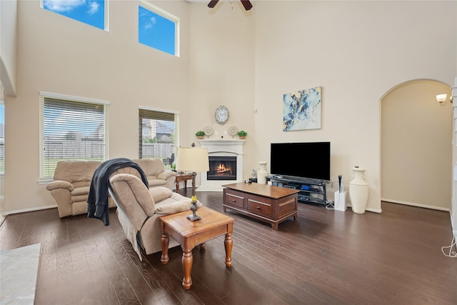 living room with ceiling fan, a towering ceiling, and dark wood-type flooring