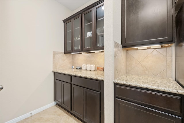 kitchen featuring dark brown cabinetry, decorative backsplash, light tile patterned floors, and light stone countertops