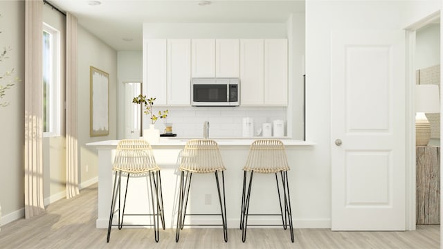 kitchen featuring a kitchen breakfast bar, white cabinetry, decorative backsplash, and light hardwood / wood-style flooring