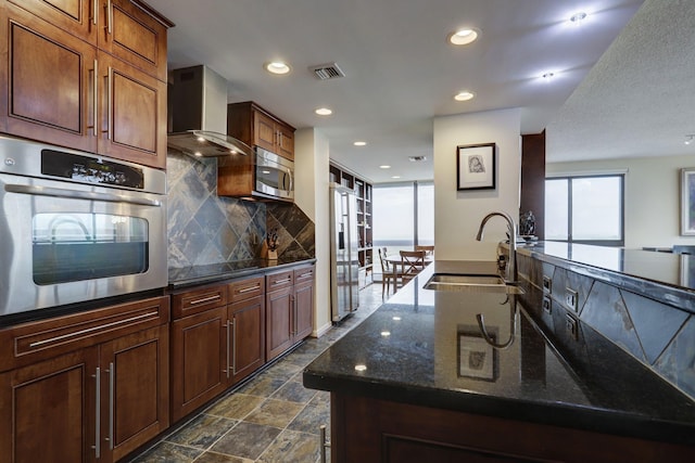 kitchen featuring a wealth of natural light, sink, wall chimney exhaust hood, backsplash, and appliances with stainless steel finishes